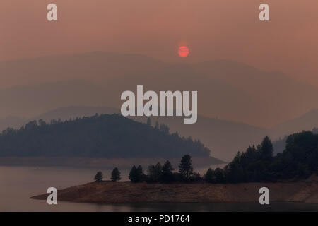 Der Rauch aus Wildfeuer erfüllte den Himmel mit untergehenden Sonnenstrahlen über dem Shasta Lake während des Carr-Feuers in der Nähe von Redding, Kalifornien Stockfoto