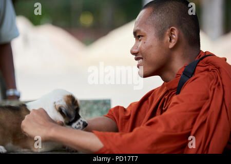 Ein Smilling junger buddhistischer Mönch spielt mit einem 2 Monate alten Welpen im Kloster, wo er lebt. In Siem Reap, Kambodscha. Stockfoto