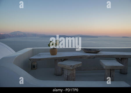 Weiß getünchtes Haus auf der Klippe mit Blick aufs Meer, Tisch und winzige Orange Baum bei Sonnenuntergang in Oia, Santorini, Kykladen, Griechenland Stockfoto