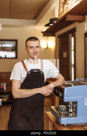 Einen fröhlichen Barista stützte sich auf die Kaffeemaschine im Cafe Stockfoto