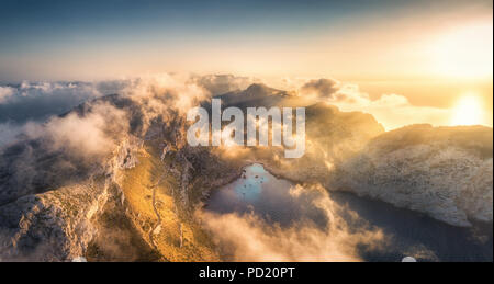 Antenne Panoramablick auf die Landschaft mit wunderschönen Bergen mit grünen Bäumen, blaues Meer und niedrige Wolken und gold Sonnenlicht bei Sonnenuntergang im Sommer in Spanien. Top Stockfoto