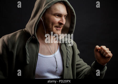 Fröhlicher junger Mann in Grün hoodie Musik beim Joggen. Seitenansicht erschossen. Hobby. Tun morgen Übung Stockfoto