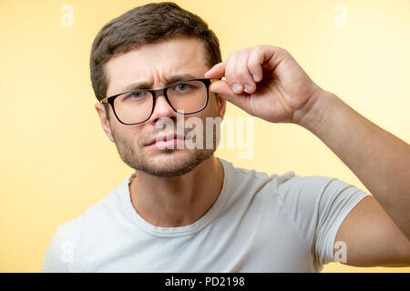 Nahaufnahme Portrait von schielen Mann mit Brille auf dem gelben Hintergrund isoliert. schlechtes Sehvermögen. Mann nicht die Beweise für seine Augen vermuten. sceptica Stockfoto