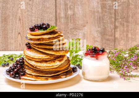 Pfannkuchen mit schwarzen Johannisbeeren, Beeren und Joghurt auf hölzernen Hintergrund Stockfoto