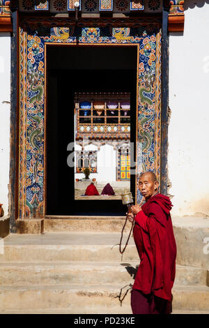 Ein Mönch Spaziergänge durch den Eingang des Kenchosum Lhakhang (Kloster) in Jakar während seine Gebetsmühle und Perlen. Bumthang Bezirk. Bhutan. Stockfoto