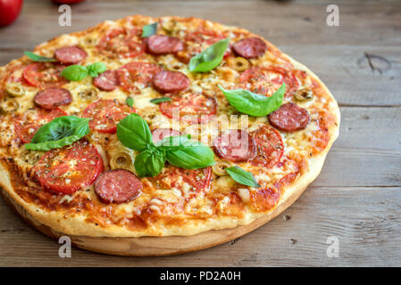 Italienische Pizza mit Tomaten, Salami, grüne Oliven, Käse und Basilikum auf hölzernen Tisch. Frische, hausgemachte Pizza, kopieren. Stockfoto