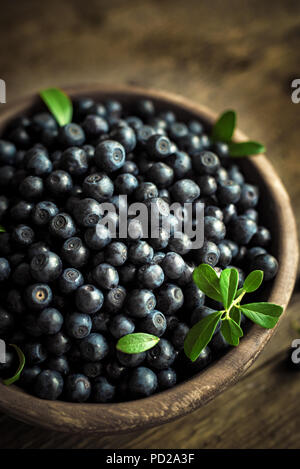 Frische Heidelbeeren mit grünen Blättern in Houten, organische Blueberry auf Holz- Hintergrund. Stockfoto
