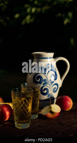 Traditionelle apple Wein in der Stadt Frankfurt am Main in Hessen. Einen Krug Wein ist auf einer alten hölzernen Tisch in den Garten, um ihn herum sind Äpfel Stockfoto