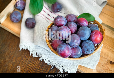 Auf der Tabelle auf eine Serviette Weidenkorb mit Reifen große Pflaumen gefüllt. Stockfoto