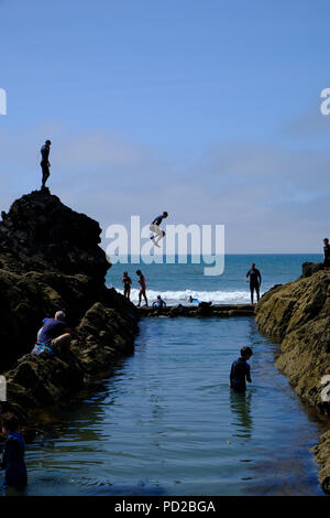 Bude, Cornwall, UK. Urlauber ins Meer springen von Felsen in einem natürlichen Pool, die Teilnahme an einem Sport bekannt als grabsteineffekt Stockfoto