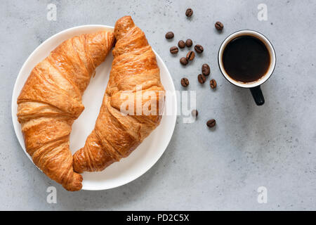 Croissants mit Kaffee. Zwei französische Croissants auf dem Teller und Tasse Espresso Kaffee auf konkreten Hintergrund, Ansicht von oben Stockfoto