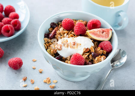 Müsli mit Joghurt, Beeren und Früchte in der Schüssel. Gesund leckeres Frühstück mit Joghurt, hausgemachtes Müsli, frisch Himbeeren und Feigen. Tasse grünen Tee o Stockfoto