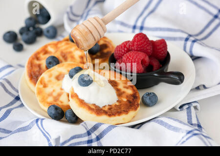 Quark Pfannkuchen oder sirniki mit saurer Sahne, Honig und Beeren. Detailansicht, selektive konzentrieren. Russische Küche Stockfoto