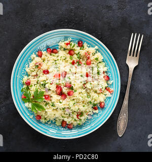 Tabbouleh Salat mit Couscous und Granatapfel Samen auf einem blauen Schild auf schwarzem Stein. Ansicht von oben, Quadrat Erntegut Stockfoto