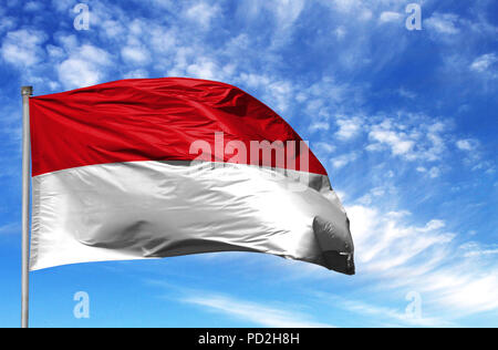 Nationalflagge von Monaco an einem Fahnenmast vor blauem Himmel. Stockfoto