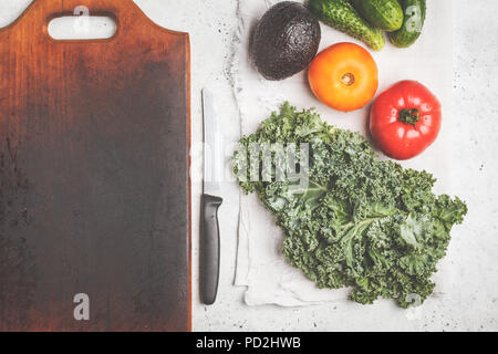 Zutaten für einen gesunden Salat auf einem weißen Tisch, Ansicht von oben. Kochen von Gemüse Salat aus Tomaten, Gurken, Avocado und Kale. Gesunde vegane Ernährung Stockfoto