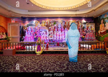 Eine Frau allein beten und meditieren vor dem Altar mit farbenfrohen Statuen von hinduistischen Gottheiten. In der Tulsi Mandir in South Richmond Hill Queens. Stockfoto