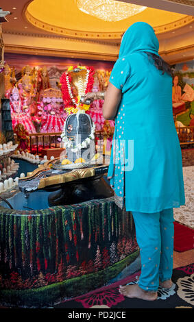 Eine Frau gießt Milch auf die Statue der Gottheit Shiva zu einem Hindu Tempel in South Richmond Hill, Queens, New York. Stockfoto