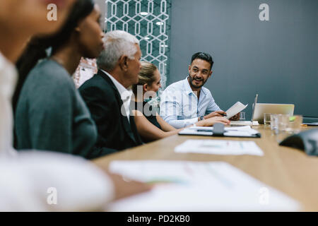 Positive junger Mann mit Team von multi-ethnischen Menschen diskutieren produktive Strategie im Sitzungssaal. Executive liest einen Bericht für das Business Team in Mee Stockfoto