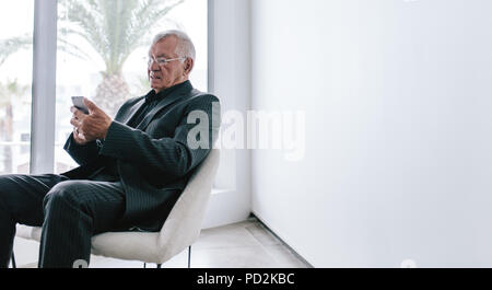 Reife Unternehmer sitzen im Foyer lesen SMS auf sein Handy. Senior Executive Sie Ihr Smartphone während der Arbeit brechen. Stockfoto