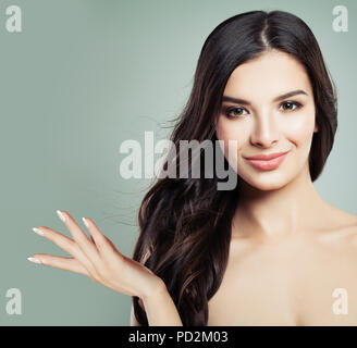 Glückliche Frau mit perfekter Haut und Lange lockige Frisur zeigt Leere Kopie auf die offene Hand. Product Placement und Werbung Marketing Konzept Stockfoto