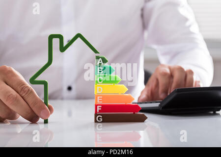 Close-up ein Geschäftsmann mit Taschenrechner holding Umrisse von Haus Modell mit Energieeffizienz rate Stockfoto