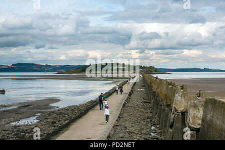 Menschen zu Fuß auf Gezeiten Causeway in Cramond Insel mit dem Zweiten Weltkrieg anti Schiff Barriere mit Resten von verschlissenen Betonmasten, Edinburgh, Schottland, Großbritannien Stockfoto