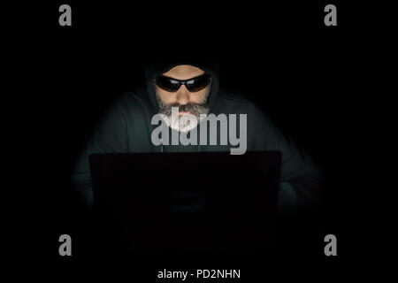 Portrait eines bärtigen computer Hacker in einem mit Laptop Hoodie in einem dunklen Raum. Stockfoto