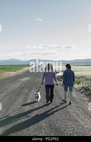 Eine Mutter und Tochter gehen ihren Zwergschnauzer auf einer Schotterstraße im Norden von Idaho.