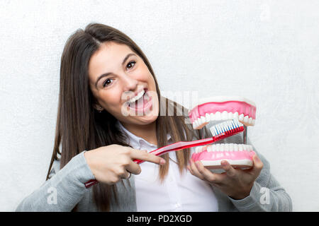 In der Nähe von Spaß Portrait von attraktiven jungen Mädchen mit überdimensionalen menschlichen Zähnen Prothese. Frau Reinigung der Zähne mit der Zahnbürste Prothese gegen lig Stockfoto