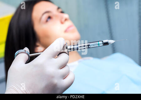 Makro Nahaufnahme einer Hand mit Handschuh Holding medizinische Spritze mit out of focus Patient im Hintergrund. Stockfoto