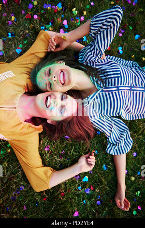 Zwei junge Frauen, farbige Kreide Pulver auf Gras im Holi Festival Lügen bedeckt, Overhead portrait Stockfoto