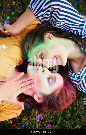 Zwei junge Frauen, farbige Kreide Pulver auf Gras im Holi Festival liegend, Ansicht von oben Stockfoto