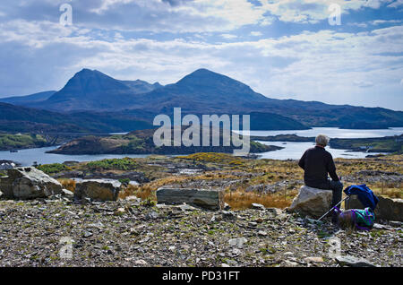 Wanderer, die sich auf Rock am Rand von rauhem steinigen Pfad mit Blick auf Meer Loch zu Quinag, Kylesku Brücke auf der linken Seite, Sutherland, Scottish Highlands. Stockfoto