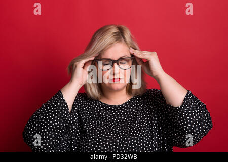 Eine übergewichtige Frau in Studio, Tempel Berühren mit den Händen wegen der Kopfschmerzen. Stockfoto