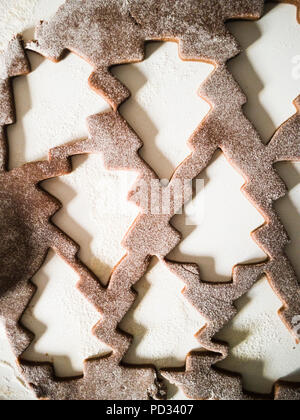 Close-up von rohem Teig Fräser mit Bohrungen in einer Form von Weihnachtsbäumen, auf weißem Hintergrund mit Mehl um. Raw Lebkuchen Teig. Stockfoto