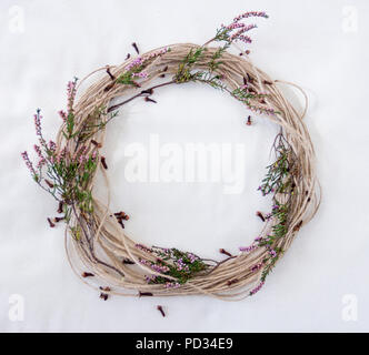 Hessischen, Garn, Jute string Kranz mit violetten und grünen Heidekraut (Erica) Zweige und braun Nelken auf rohen Baumwollgewebe ecru Hintergrund Stockfoto