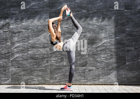 Junge fitness Frau tun, Warm-up-Training bevor sie ihr Bein ausdehnen, indem sie Knie zur Brust Strecke auf der Straße der Stadt. Sportliche Athlet pr Stockfoto