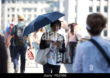 London, UK, 6. August 2018, eine asiatische Frau schützt sie sich vor der Sonne mit einem Regenschirm als Sie über London Bridge geht. Die Wettervorhersage ist heiß und sonnig bis Mittwoch, wenn es kühler geworden ist, wird eine willkommene Entlastung für einige Leute werden. Kredit Keith Larby/Alamy leben Nachrichten Stockfoto