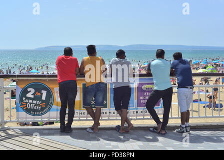 Eine Gruppe junger Männer, die über den Strand von der Seebrücke während der Sommerhitze 2018, Bournemouth, Dorset, Großbritannien Stockfoto