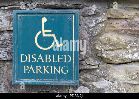 Behinderte Parken Schild mit gelber Text und der Mensch Person im Rollstuhl Symbol mit grünem Hintergrund auf einer alten Steinmauer Stockfoto