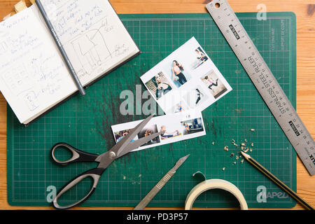 Top down Sicht der Schneidematte mit Skizzenbuch, Schere, Klebeband, Lineal, Drucke und Bleistift. Stockfoto
