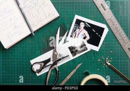 Top down Sicht der Schneidematte mit Skizzenbuch, Schere, Klebeband, Lineal, Drucke und Bleistift. Stockfoto