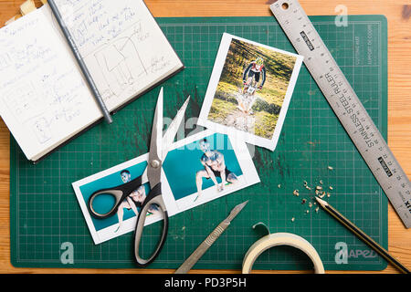 Top down Sicht der Schneidematte mit Skizzenbuch, Schere, Klebeband, Lineal, Drucke und Bleistift. Stockfoto