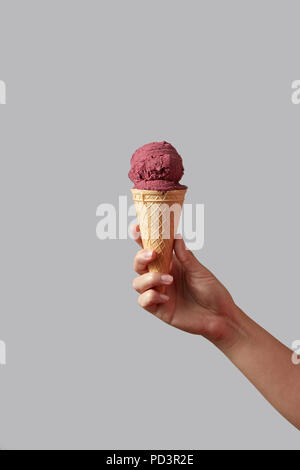 Eine weibliche Hand hält rote Beere Eis in der Waffel Kegel auf einem hellgrauen Hintergrund. Stockfoto