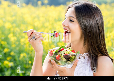 Nahaufnahme Gesicht geschossen von attraktiven gesunde Mädchen Salat im Freien mit Blume Bereich im Hintergrund. Stockfoto