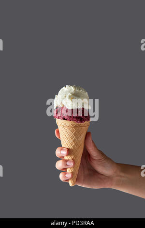 Eine Waffel Kegel mit roter Kirsche und weiße Milch Eis. Weibliche Hand hält Waffel Kegel auf einem grauen Hintergrund. Platz für Text. Stockfoto