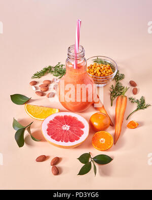 Gesundes Frühstück ogange Smoothie aus Zitrusfrüchten, Sanddorn, Karotte, Mandeln in einer Glasschüssel auf orangefarbenem Papier Hintergrund. Stockfoto