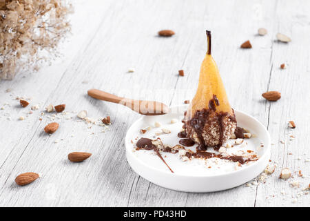 Birne in Schokolade und Mandeln auf einem weissen Teller, auf einer hölzernen weißen Hintergrund. Stockfoto