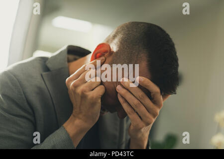 Nahaufnahme eines Leidens kaukasischen Mann mit einer Hand in seinem Kopf und mit der anderen Hand über sein Ohr Stockfoto